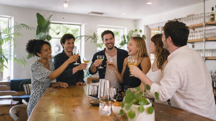 Feiernde Gruppe stößt in einer hellen Bar mit Holztheke an, Beispiel für eine Bar zum Mieten