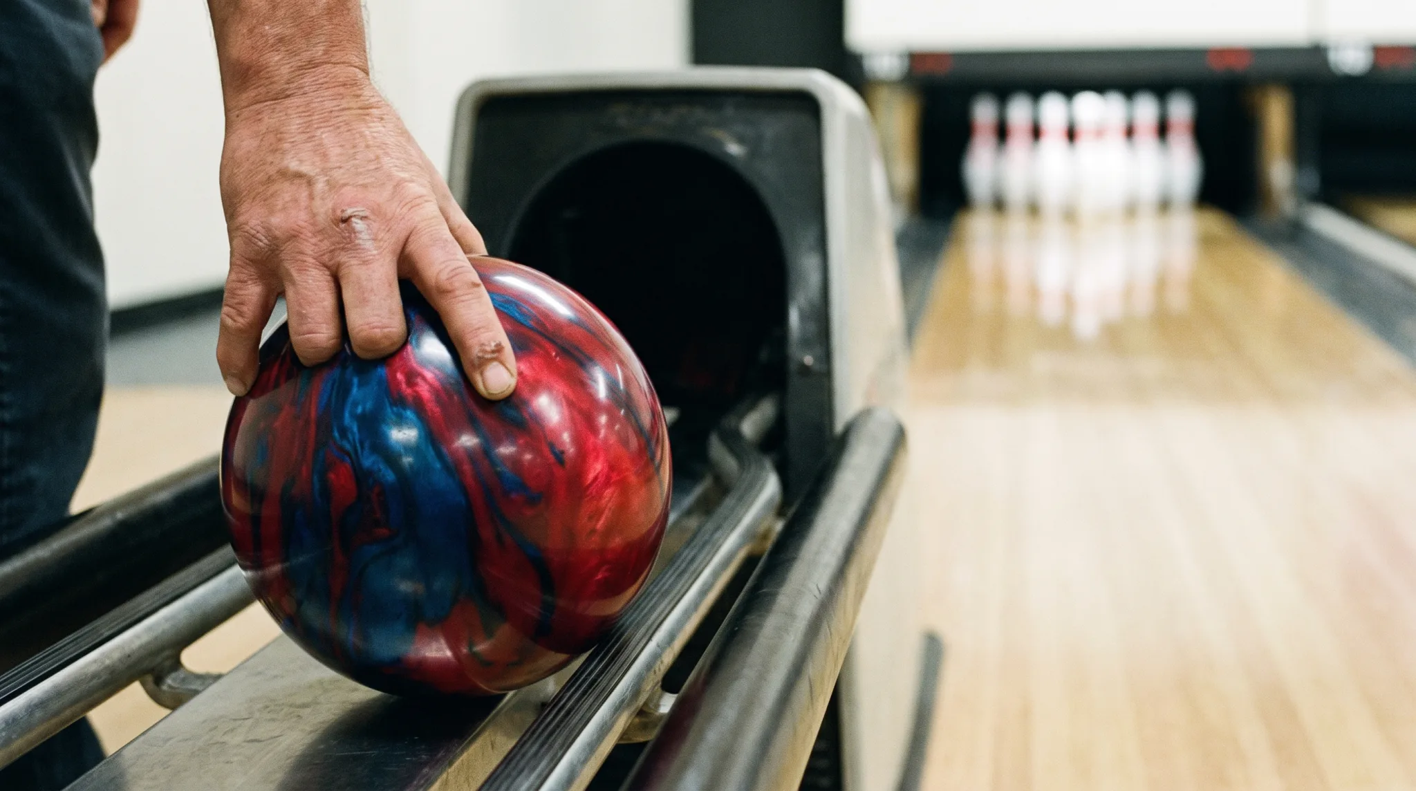 Hand mit marmorierter Bowlingkugel vor den Pins auf der Bahn