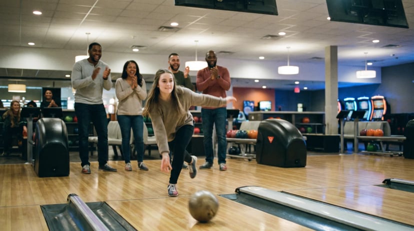 Gruppe feiert gemeinsam beim Bowling, eine Spielerin wirft gerade die Kugel