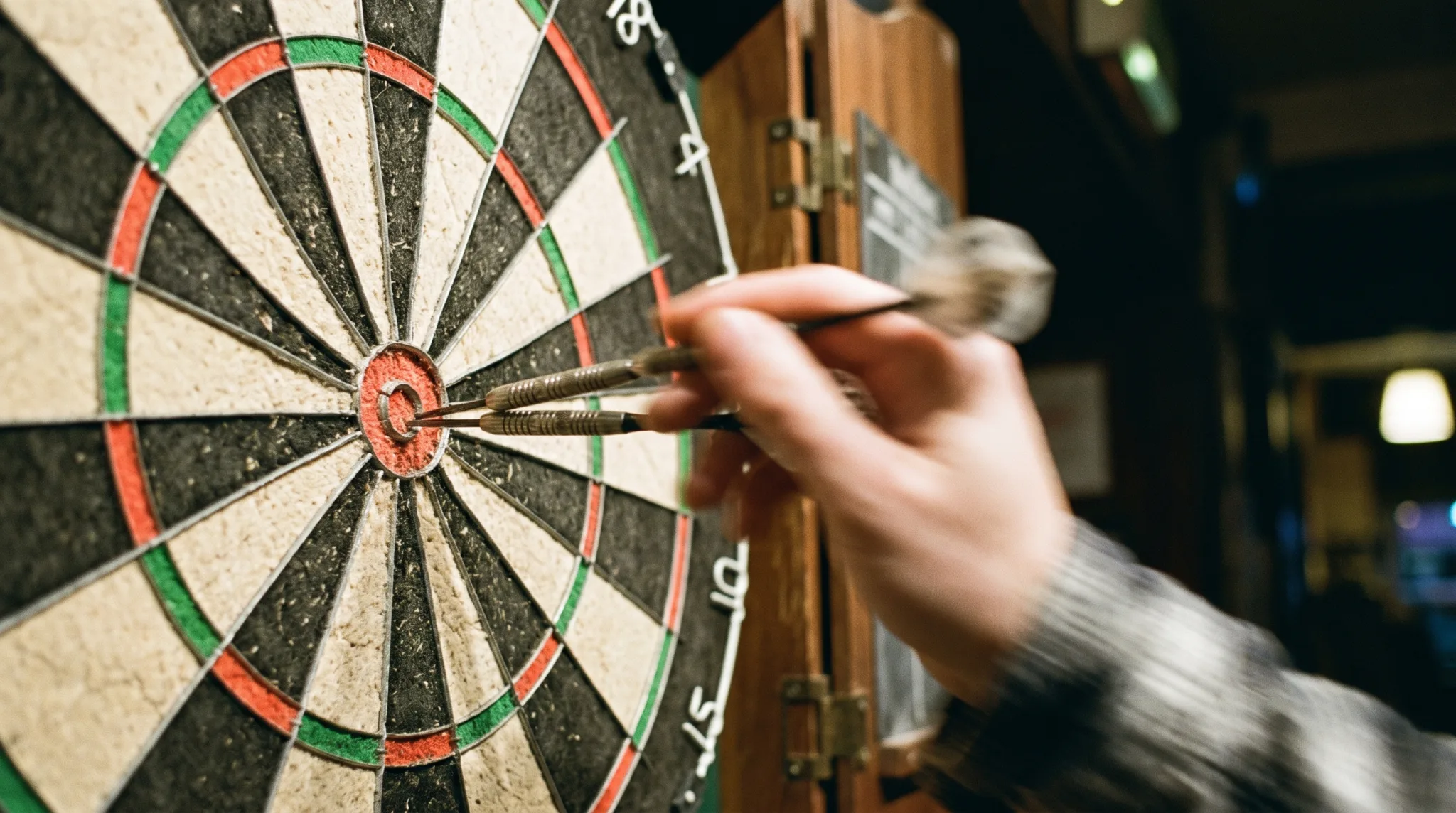 Drei Darts nahe dem Bullseye einer Dartscheibe, Hand wirft