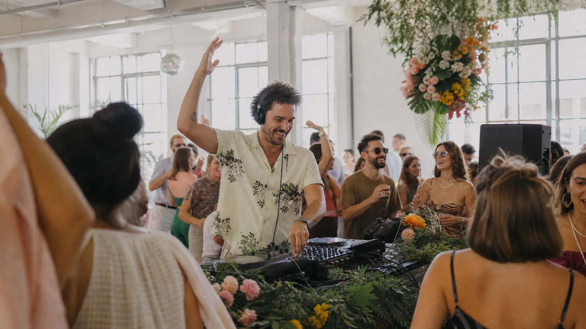 DJ legt bei einer hellen Feier auf, während Gäste tanzen, Beispiel für einen DJ für euer Event