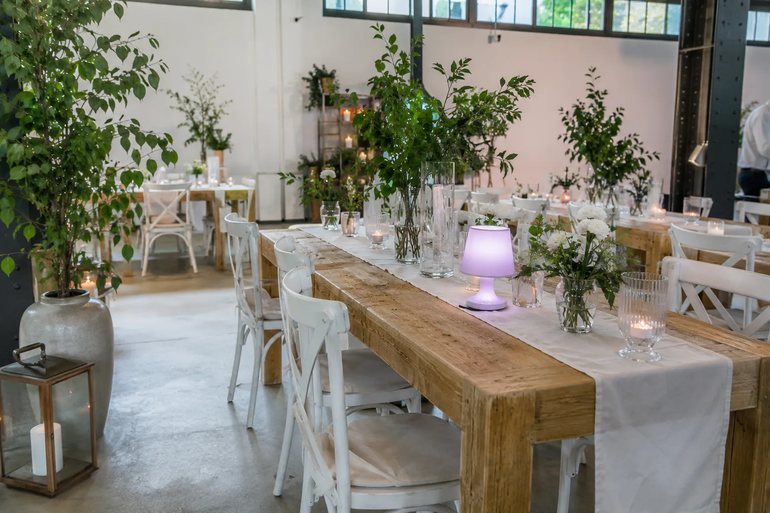 Eventausstattung in einem hellen Loft in Much mit langer Holztafel, weißen Stühlen und Kerzendekoration