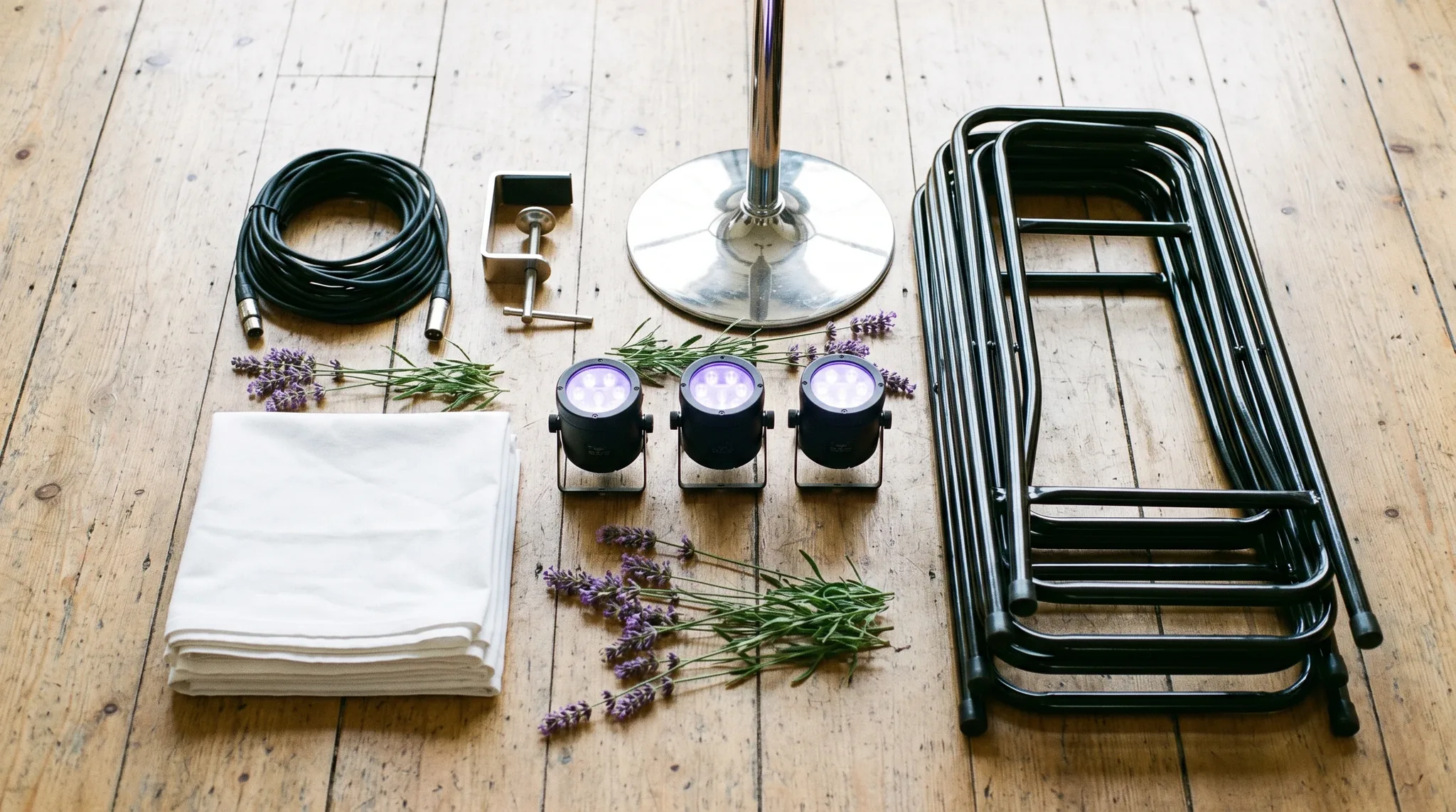 Eventausstattung in Troisdorf: Flatlay mit gestapelten Stuhlschleifen, einem Tischläufer in Rosé, LED-Kerzen und einem aufgerollten Verlängerungskabel auf.