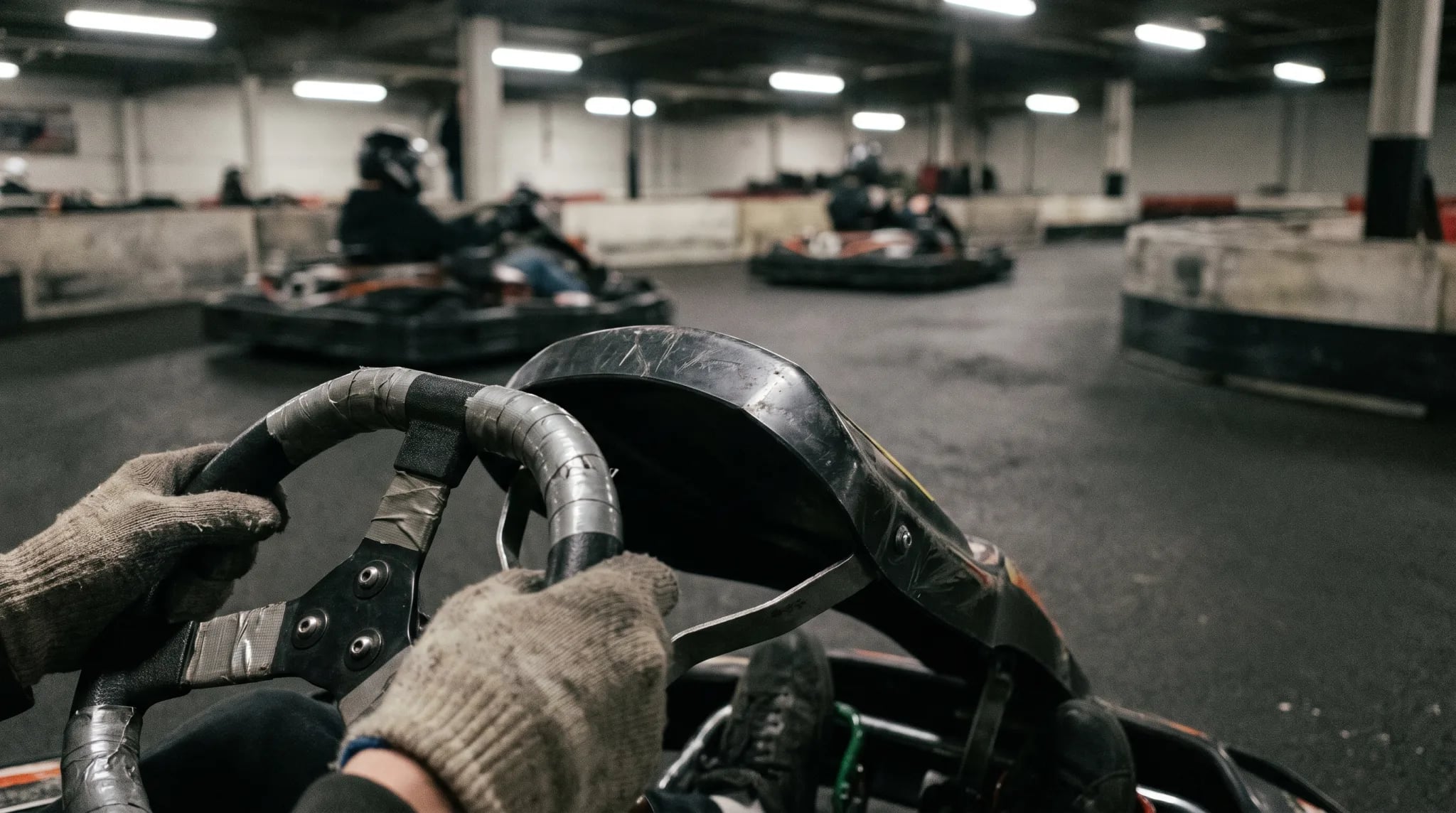Behandschuhte Hände am Lenkrad eines Gokarts auf der Bahn