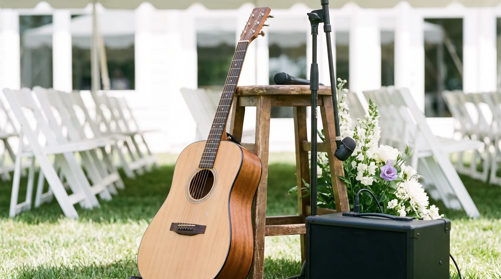 Hochzeitsband Details: Akustikgitarre, Mikrofon auf Stativ und kleiner Verstärker neben Blumen für die Trauung im Garten