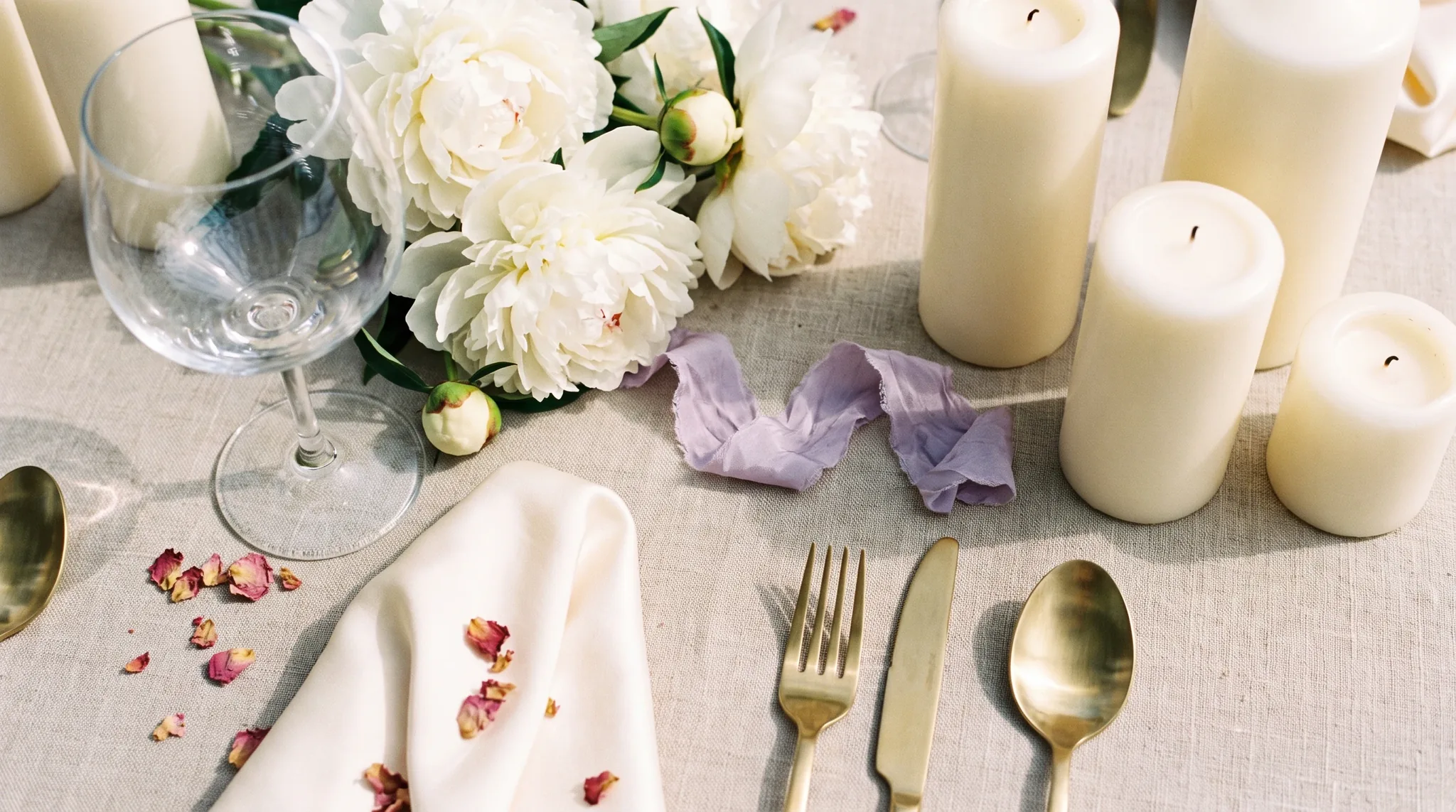Stilvolles Flat-Lay mit Kerzen, Gartenrosen, Leinenservietten und Champagnergläsern als Details einer Hochzeitslocation in Swisttal auf verwittertem Eichentisch
