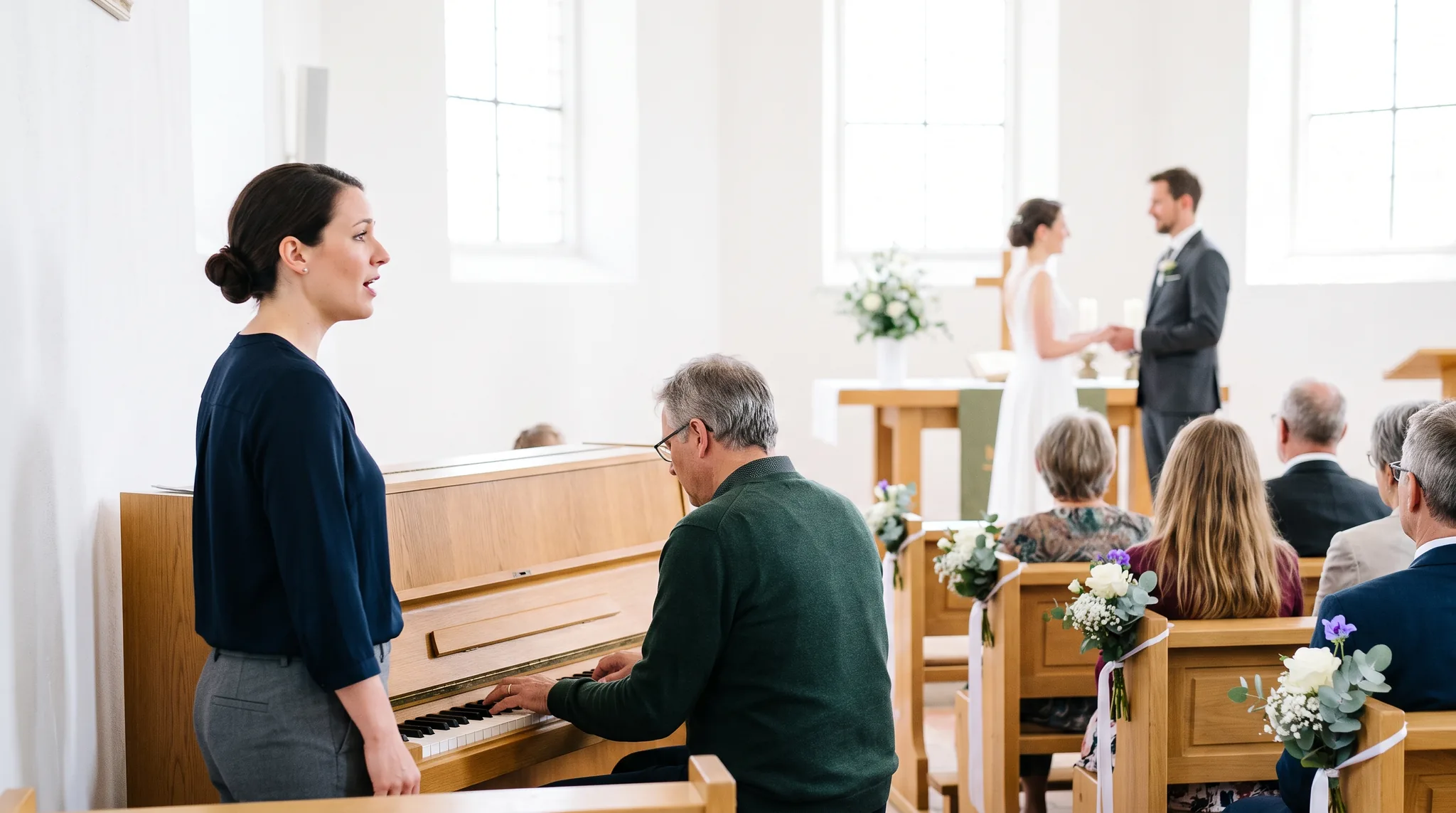 Hochzeitssängerin singt bei der Trauung in einer hellen Kirche, ein Pianist begleitet sie am Klavier, im Hintergrund steht das Brautpaar am Altar