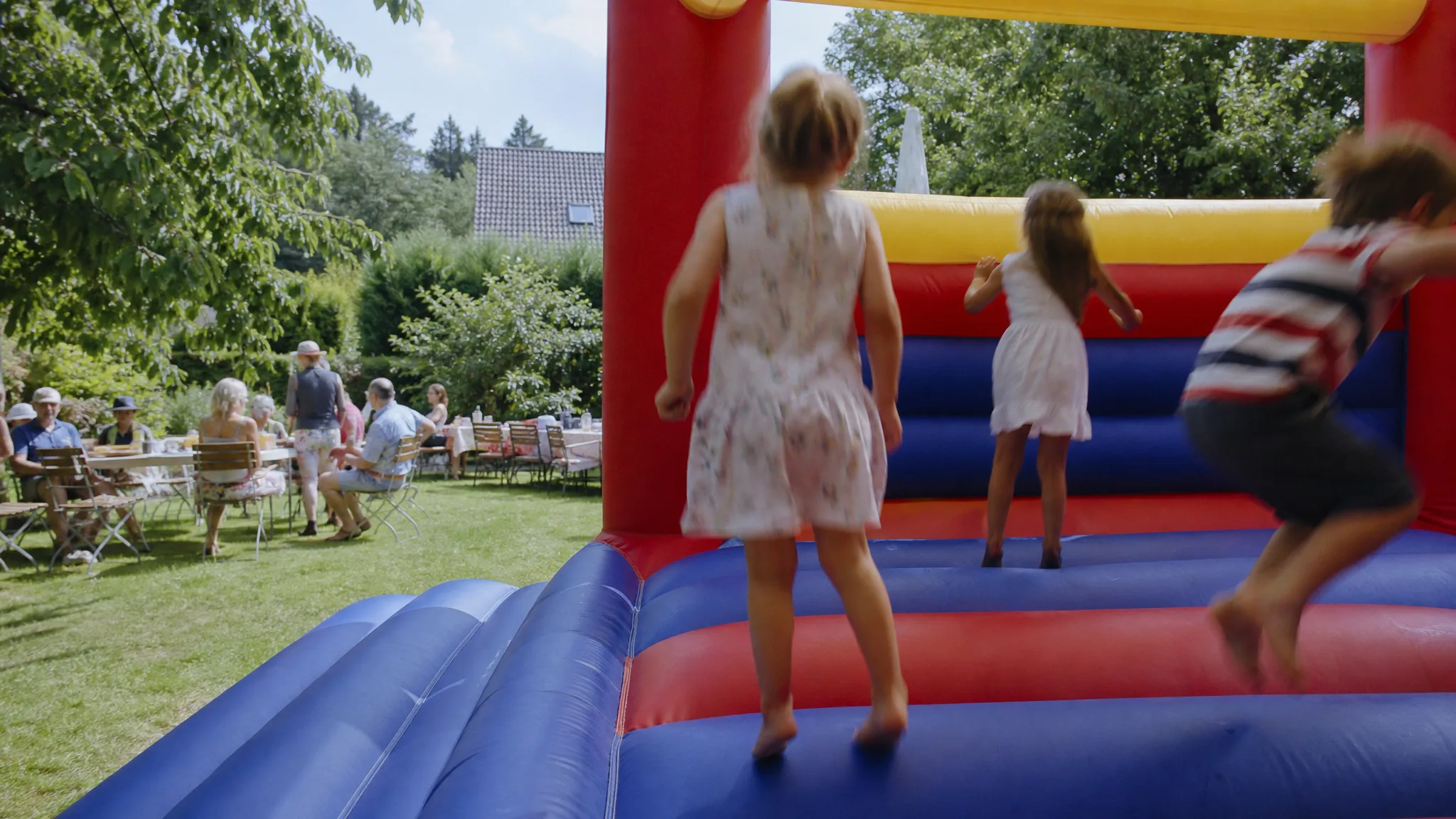Kinder springen auf einer bunten Hüpfburg bei einem Sommerfest im Garten, Hüpfburg mieten in NRW