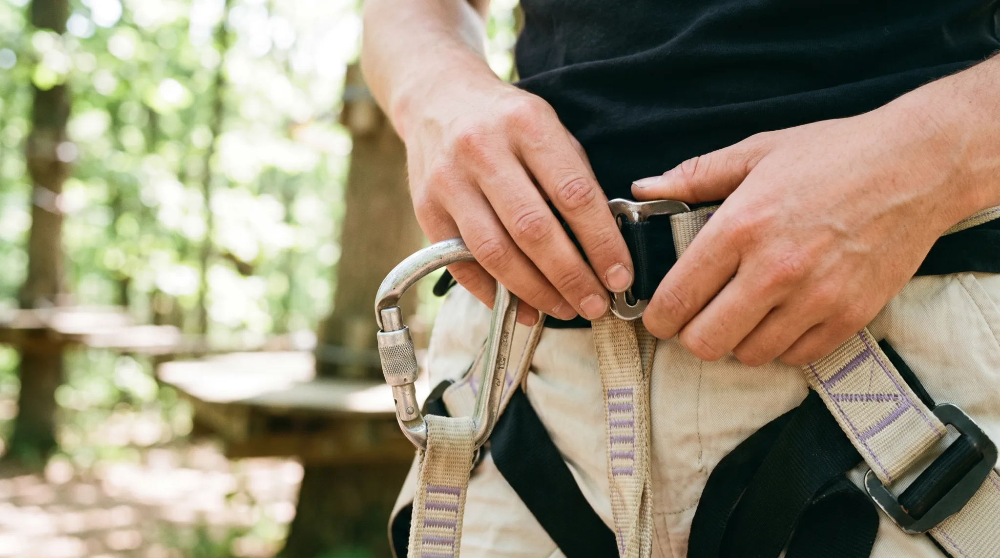 Hände sichern einen Karabiner am Stahlseil des Kletterparcours in Köln
