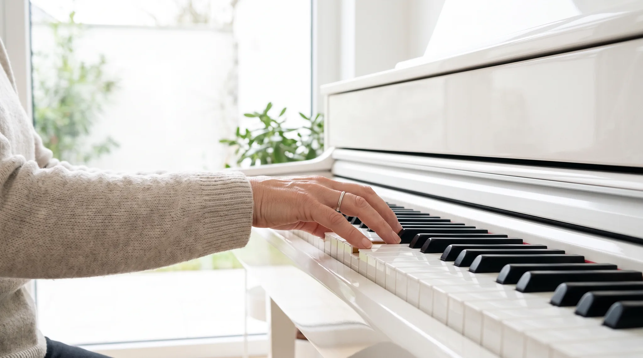Musiker Detail: Hände einer Pianistin mit silbernem Ring auf den Tasten eines weißen Klaviers am hellen Fenster